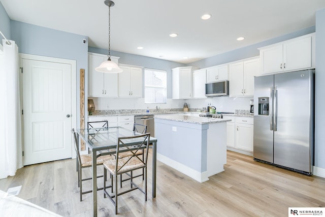 kitchen featuring stainless steel appliances, white cabinets, light wood-style floors, and hanging light fixtures