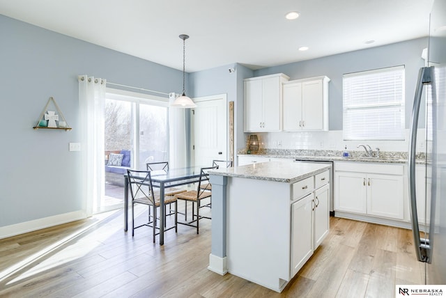 kitchen with light stone counters, a sink, a kitchen island, white cabinetry, and light wood-type flooring