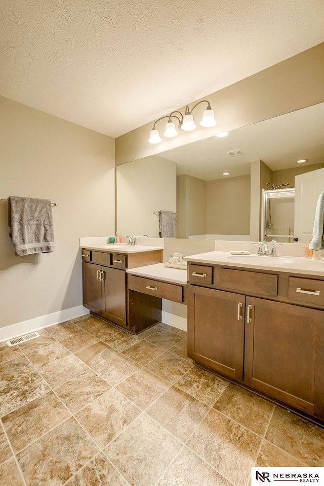 bathroom featuring baseboards, visible vents, a sink, a shower stall, and two vanities