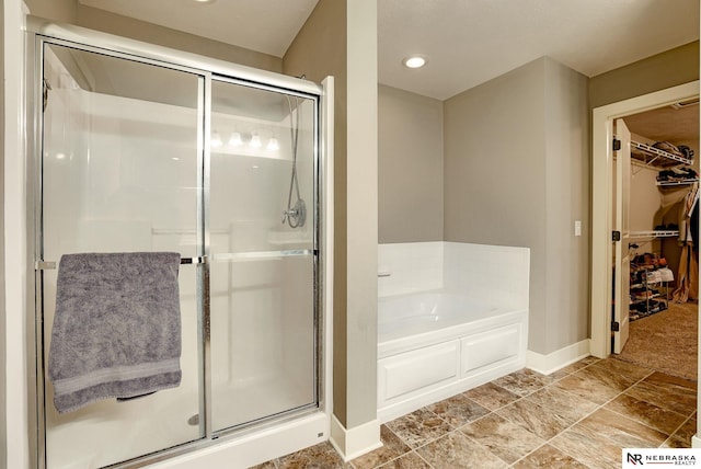 full bathroom with baseboards, a spacious closet, a shower stall, a bath, and stone finish flooring