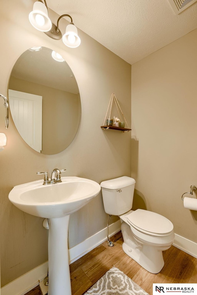 half bath featuring a textured ceiling, wood finished floors, toilet, and baseboards