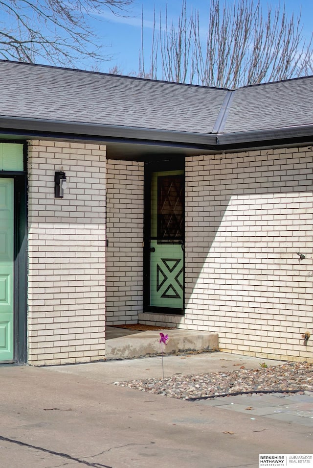 entrance to property with brick siding and a shingled roof