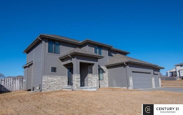 prairie-style home featuring a garage, stone siding, driveway, and fence