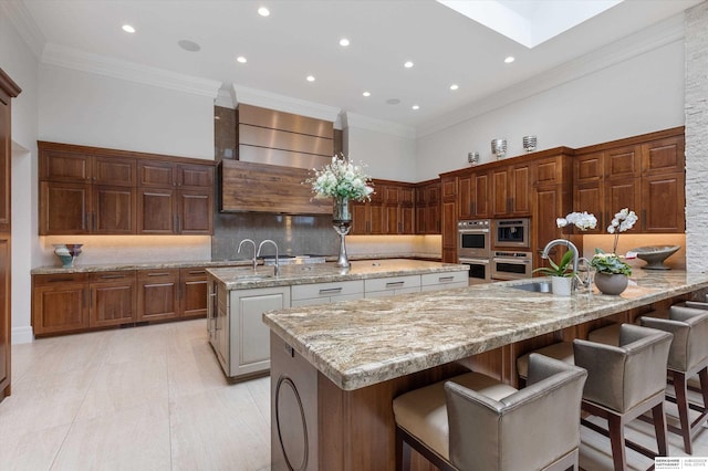 kitchen featuring a kitchen island with sink, ornamental molding, a sink, a towering ceiling, and backsplash