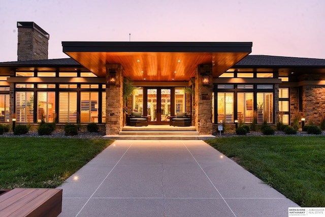 exterior entry at dusk featuring a lawn, stone siding, and a chimney