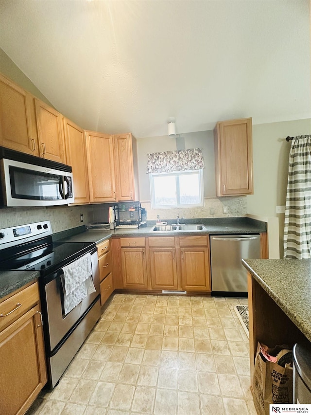 kitchen with dark countertops, light brown cabinets, appliances with stainless steel finishes, and a sink