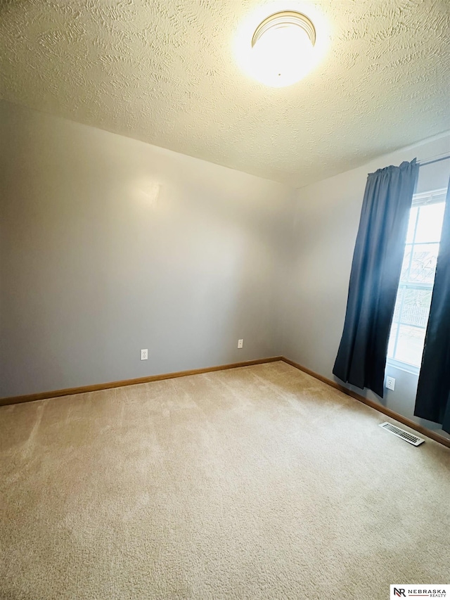 spare room featuring baseboards, visible vents, carpet floors, and a textured ceiling