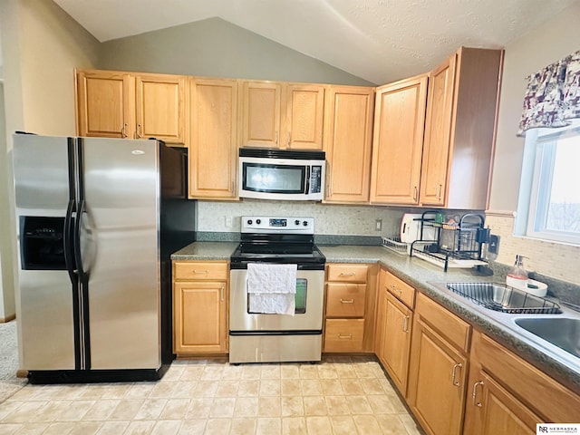 kitchen featuring light brown cabinets, decorative backsplash, appliances with stainless steel finishes, and vaulted ceiling