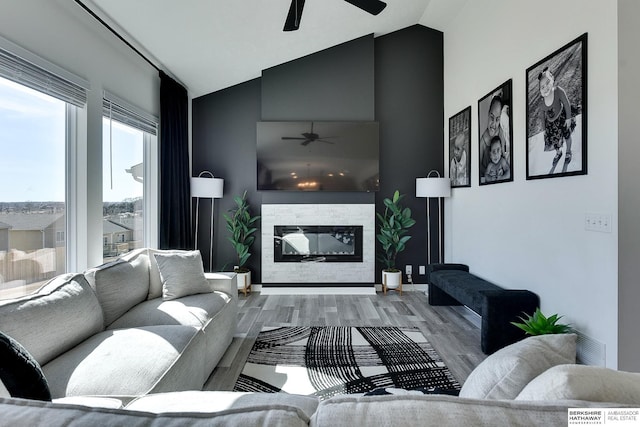 living room with a glass covered fireplace, vaulted ceiling, wood finished floors, and ceiling fan