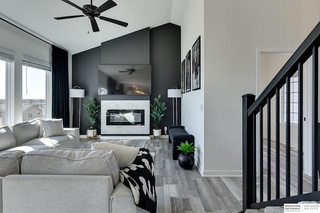 living room featuring light wood-type flooring, a ceiling fan, baseboards, a fireplace, and lofted ceiling