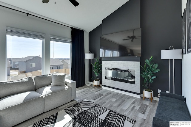 living room featuring baseboards, lofted ceiling, a fireplace, wood finished floors, and a ceiling fan