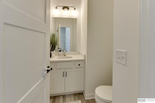 half bathroom featuring baseboards, toilet, wood finished floors, and vanity