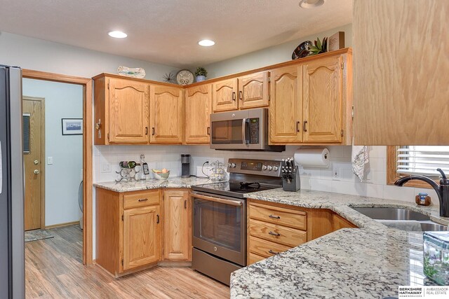 kitchen featuring tasteful backsplash, appliances with stainless steel finishes, light wood-type flooring, and a sink