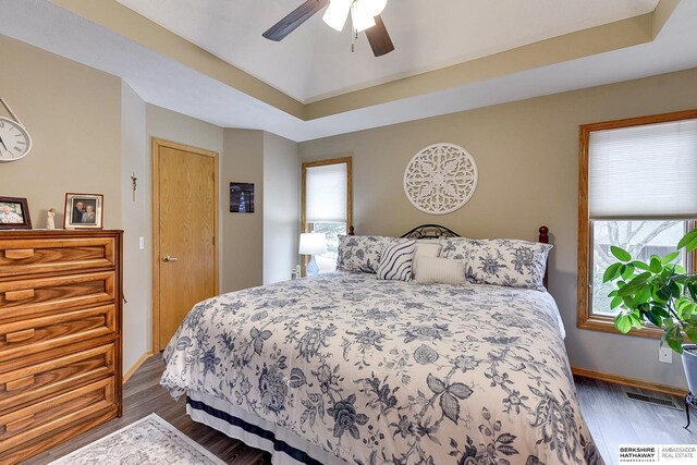 bedroom with visible vents, a raised ceiling, baseboards, and dark wood-style flooring