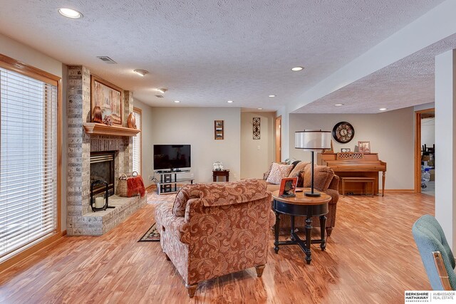 living area featuring visible vents, light wood-type flooring, recessed lighting, a fireplace, and a textured ceiling