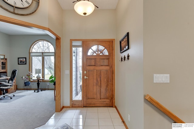 entrance foyer with light tile patterned flooring, light colored carpet, baseboards, and a towering ceiling