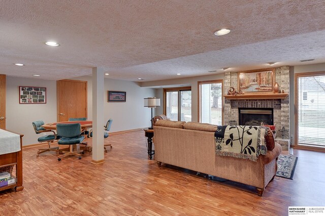 living room featuring light wood-type flooring, baseboards, a textured ceiling, and a brick fireplace