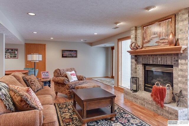 living area featuring light wood-type flooring, visible vents, a textured ceiling, recessed lighting, and a brick fireplace