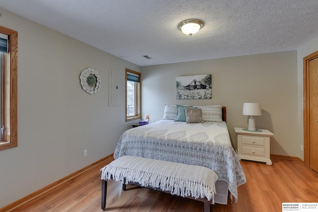 bedroom featuring visible vents, light wood-style flooring, a textured ceiling, and baseboards