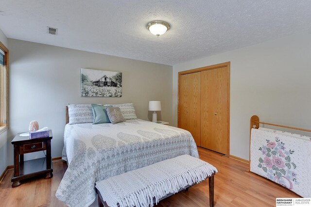 bedroom featuring baseboards, visible vents, light wood-style floors, a closet, and a textured ceiling