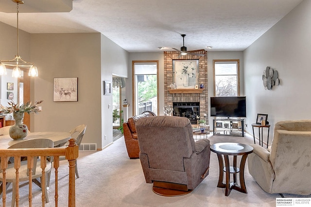 living room featuring a brick fireplace, baseboards, light colored carpet, a textured ceiling, and a ceiling fan