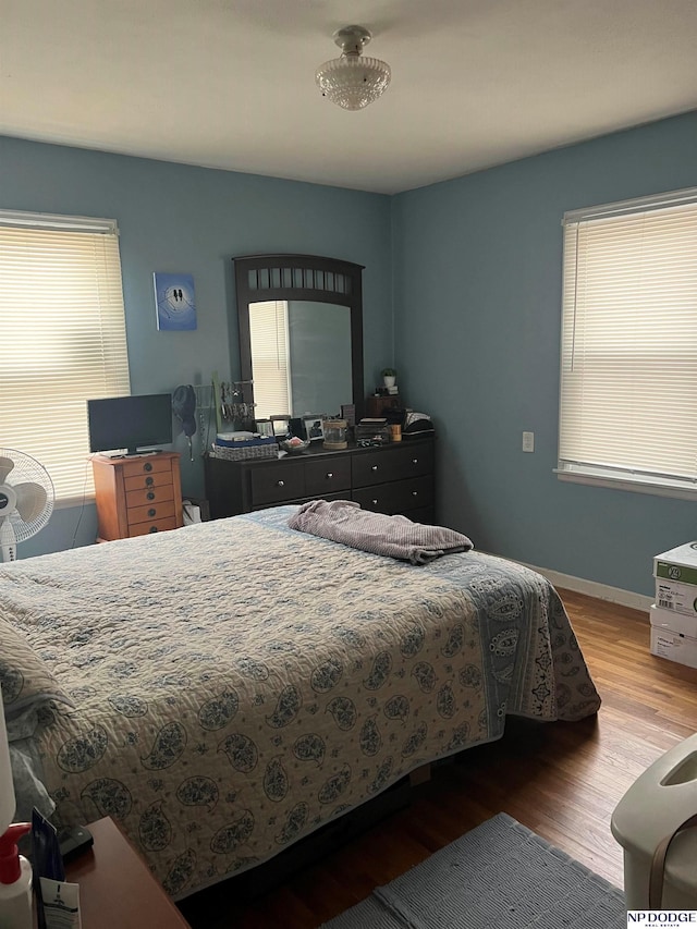 bedroom with baseboards, multiple windows, and wood finished floors