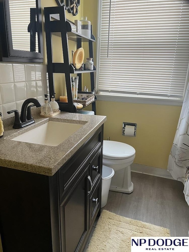 bathroom with baseboards, toilet, decorative backsplash, wood finished floors, and vanity