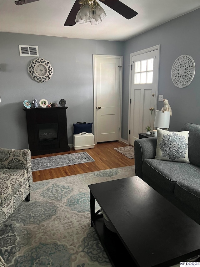 living room featuring a glass covered fireplace, wood finished floors, visible vents, and ceiling fan