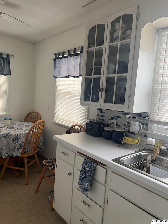 kitchen with light countertops, white cabinets, glass insert cabinets, and a sink