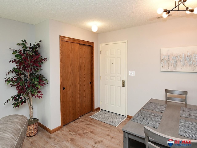 foyer featuring an inviting chandelier, light wood-style flooring, a textured ceiling, and baseboards