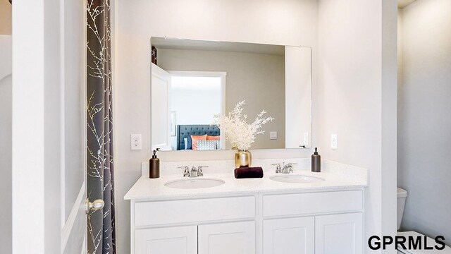 ensuite bathroom featuring ensuite bath, double vanity, toilet, and a sink