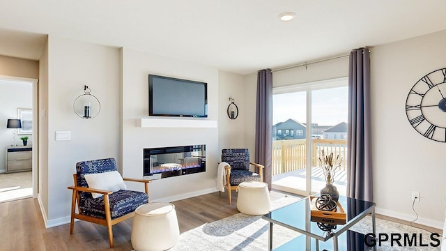 living area with baseboards, wood finished floors, and a glass covered fireplace