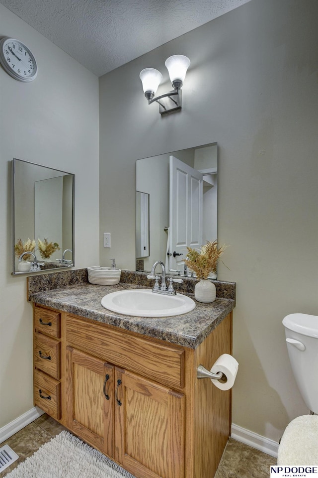 half bath with visible vents, baseboards, toilet, vanity, and a textured ceiling