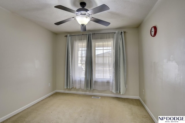 spare room featuring visible vents, baseboards, light colored carpet, a textured ceiling, and a ceiling fan