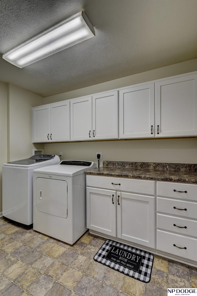 laundry area featuring a textured ceiling, stone finish floor, cabinet space, and washing machine and clothes dryer