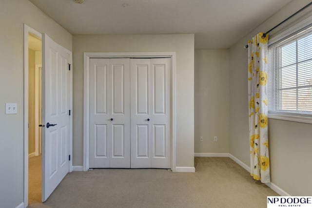 unfurnished bedroom with light colored carpet, a closet, and baseboards