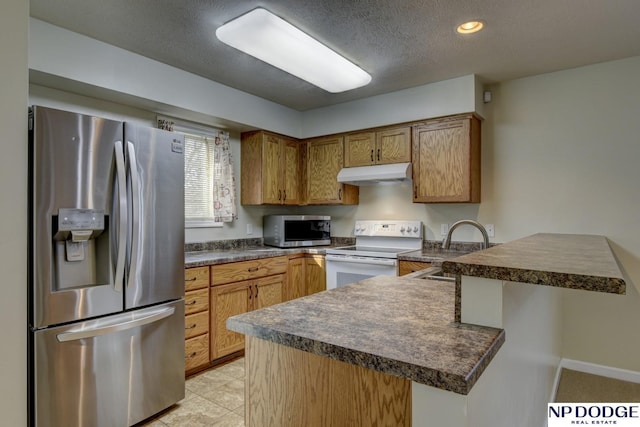 kitchen featuring a peninsula, a sink, stainless steel appliances, under cabinet range hood, and dark countertops