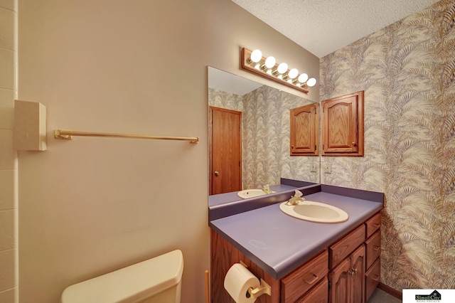 bathroom featuring toilet, a textured ceiling, wallpapered walls, and vanity