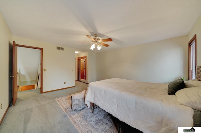 bedroom featuring visible vents, a textured ceiling, baseboards, light colored carpet, and ceiling fan