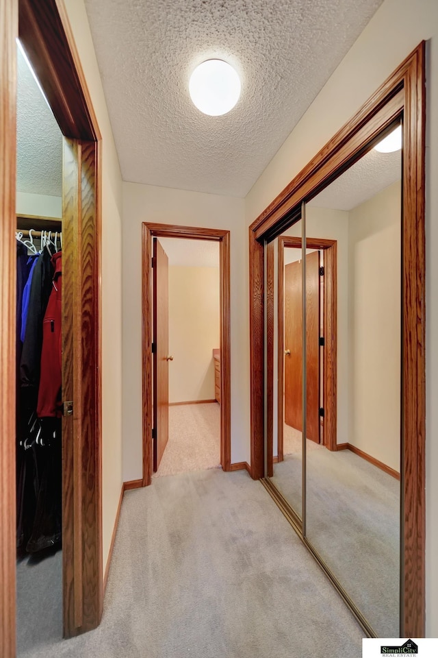 hallway with light colored carpet, baseboards, and a textured ceiling