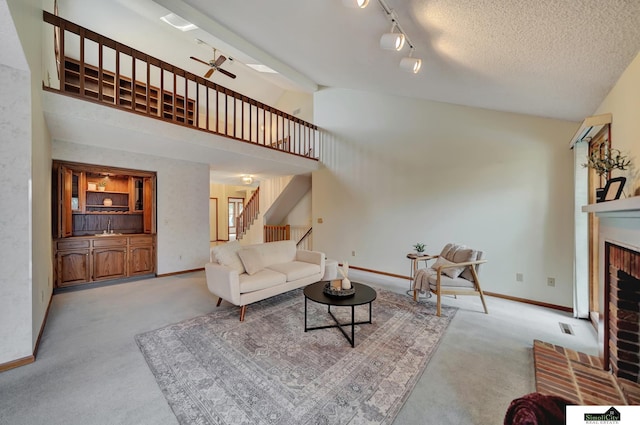 carpeted living area with stairs, a fireplace, a textured ceiling, high vaulted ceiling, and a ceiling fan