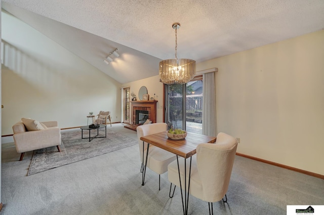 dining room featuring a brick fireplace, baseboards, vaulted ceiling, carpet floors, and a textured ceiling