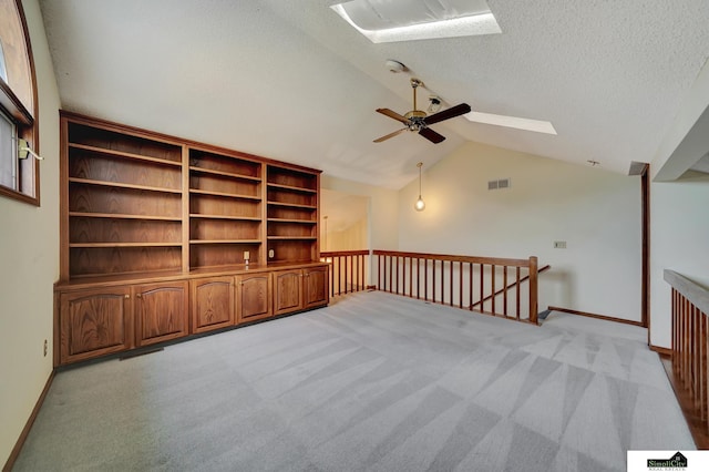 empty room with visible vents, ceiling fan, light carpet, vaulted ceiling with skylight, and a textured ceiling