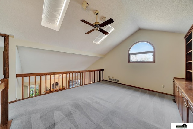 additional living space featuring visible vents, lofted ceiling with skylight, a textured ceiling, carpet floors, and ceiling fan