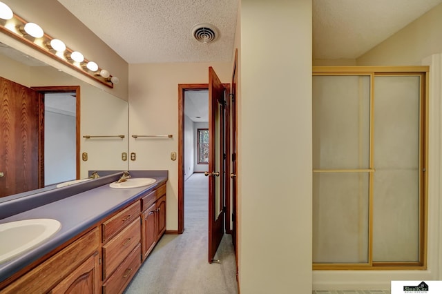 bathroom featuring a shower with door, visible vents, double vanity, a textured ceiling, and a sink