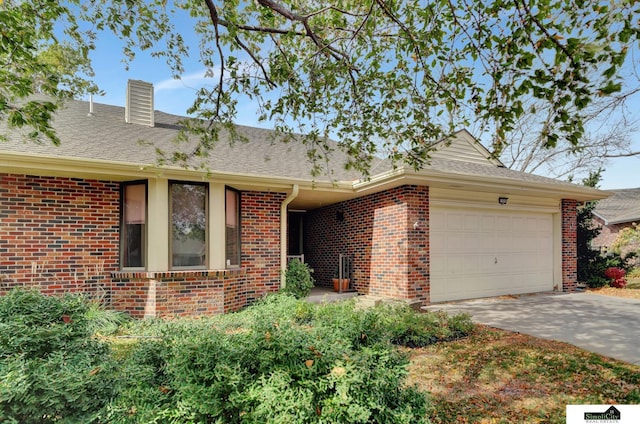 single story home featuring driveway, roof with shingles, a garage, brick siding, and a chimney