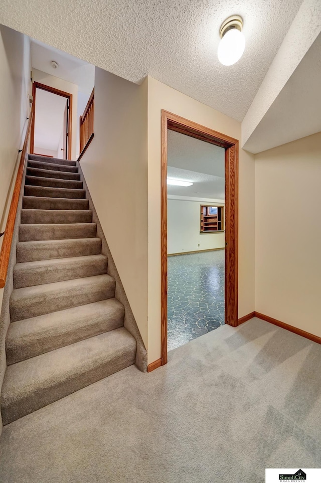 stairs with baseboards, carpet floors, and a textured ceiling