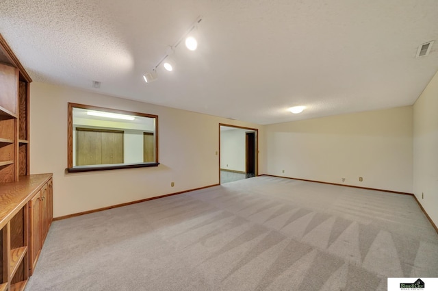 empty room featuring visible vents, light colored carpet, a textured ceiling, and baseboards