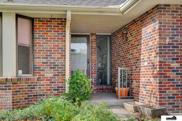 doorway to property with brick siding and roof with shingles