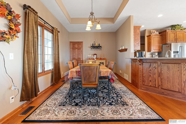 dining area with an inviting chandelier, a tray ceiling, light wood-style floors, and visible vents